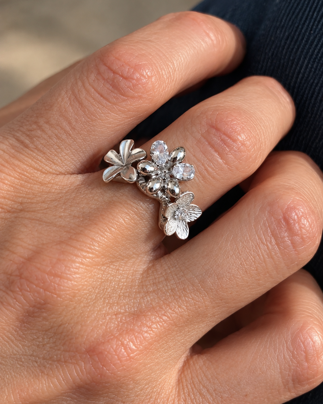 Bague fleur argentée Un matin au jardin portée à la main, en acier inoxydable finition PVD, ornée de fleurs en relief et de deux zircons.