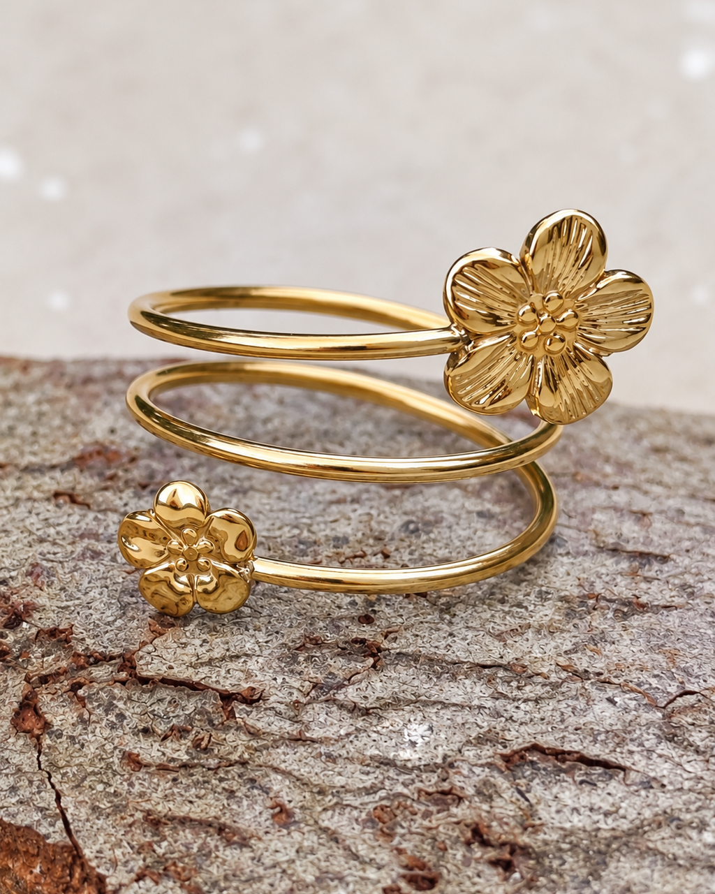 Bague fleur dorée Jardin suspendu en acier inoxydable, composée de trois anneaux ouverts et de deux fleurs en relief, présentée en gros plan.