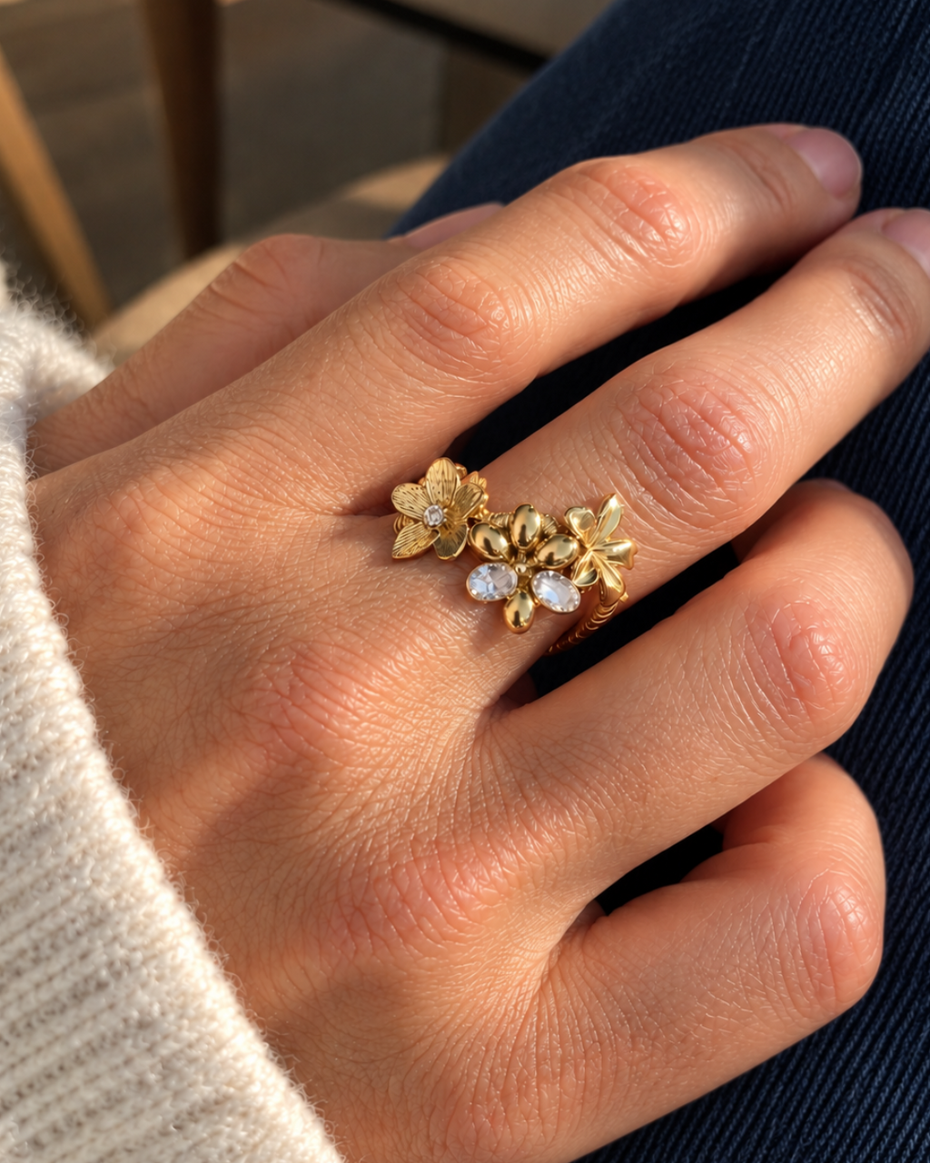Bague fleur dorée Un matin au jardin portée à la main, en acier inoxydable finition PVD, ornée de fleurs en relief et de deux zircons.