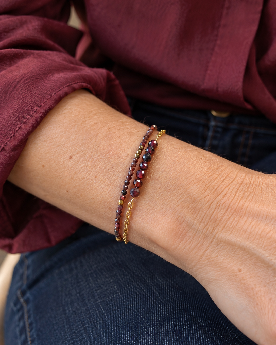 Bracelet Garance double rang porté au poignet d'une femme, composé de perles de grenat naturel facettées et de détails en plaqué or 18 carats. Bijou féminin créé et assemblé à la main en France par Yselia.