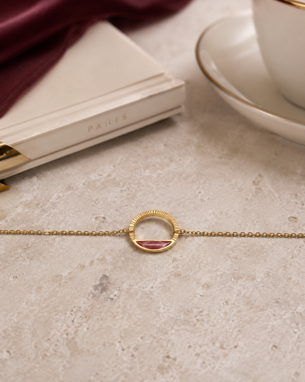 détail du bracelet Livia doré et rouge profond en acier inoxydable posé sur une table.