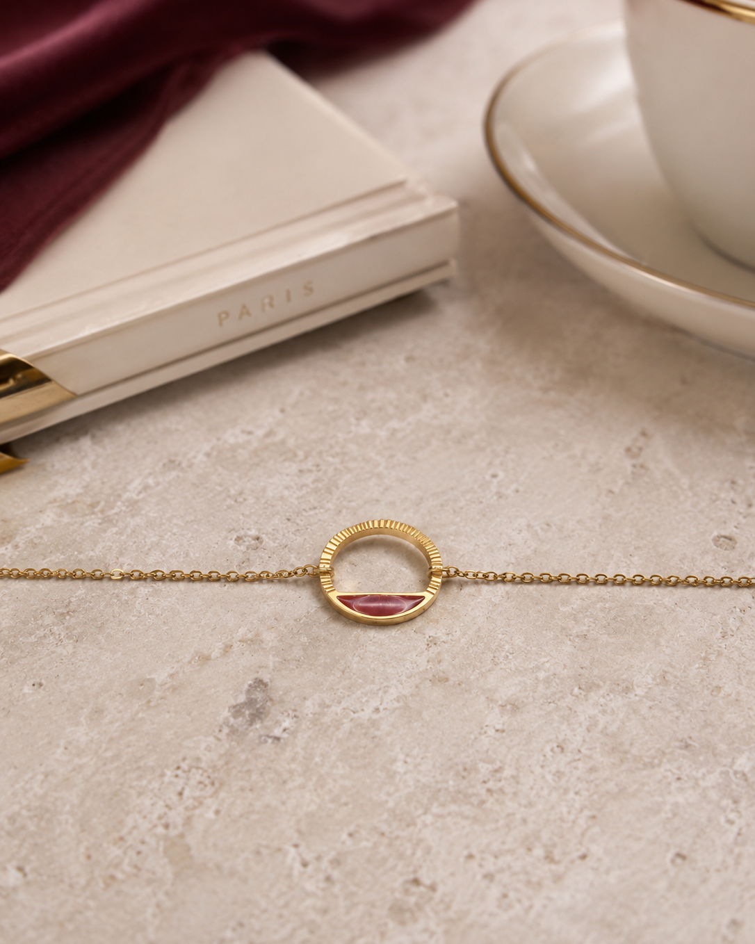 détail du bracelet Livia doré et rouge profond en acier inoxydable posé sur une table.