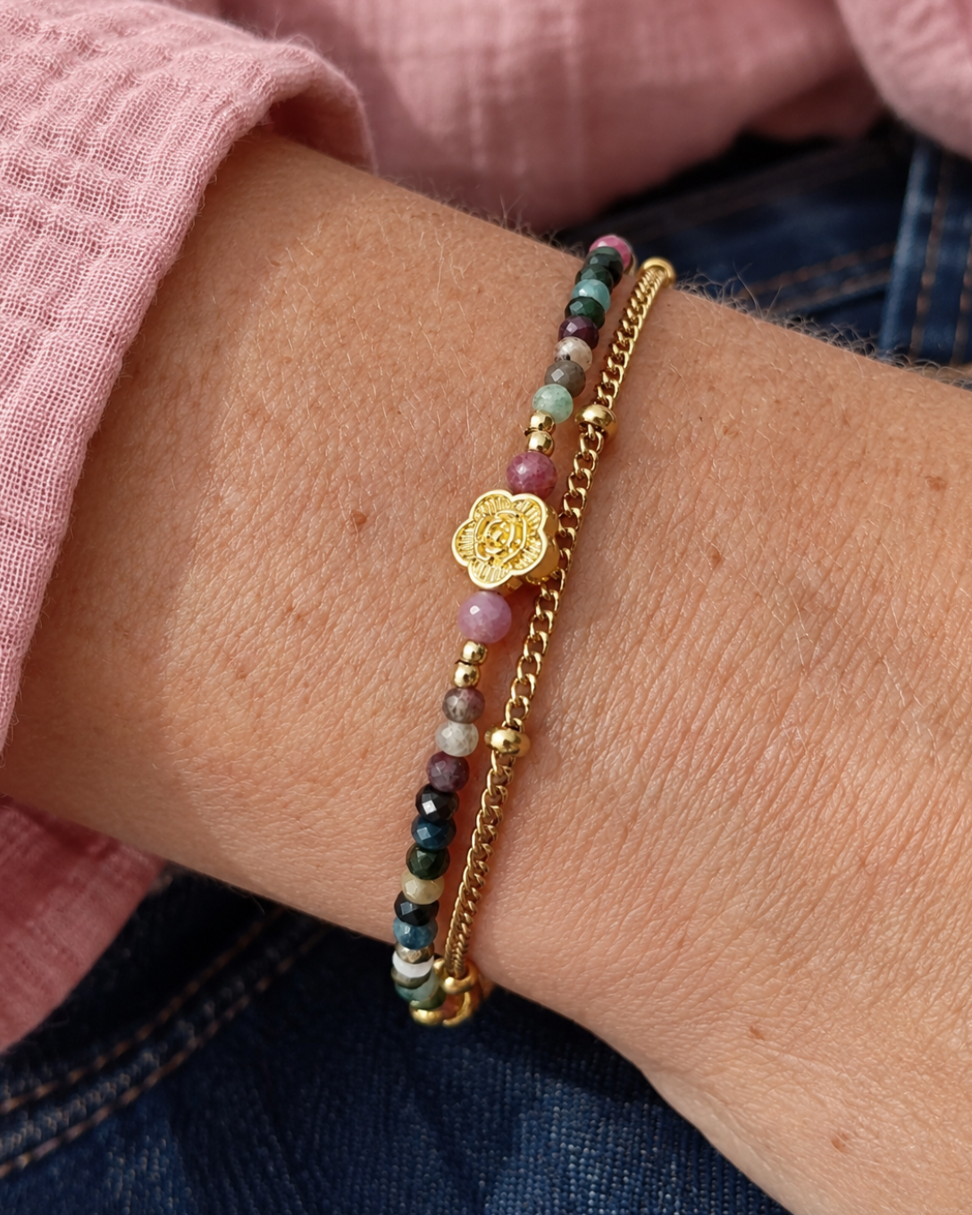 Bracelet femme double rang Monet porté au poignet, composé de tourmalines naturelles multicolores, d’une fleur dorée et d’une chaîne en plaqué or 18 carats, fait main en France.