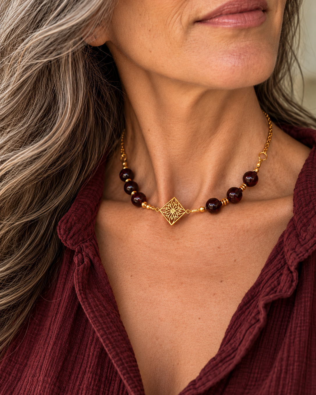 photo portée du collier Arabesque et ses perles de grenat aux nuances rouge profond. Son médaillon en plaqué or 18 carats dévoile de délicates arabesques ajourées, sublimées par de fines perles intercalaires dorées et travaillées. Un jeu de contrastes entre la profondeur des pierres naturelles et la finesse de l'or. Une création imaginée et assemblée à la main dans notre atelier en France.