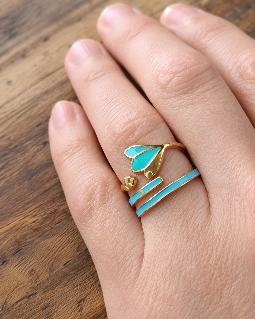 photo portée de gros plan sur le duo de bagues dorées en acier inoxydable composé d'une bague en finition laquée vert et turquoise en forme de feuille et d'un anneau en finition laquée turquoise. Cest un ensemble élégant et harmonieux sur le doigt.