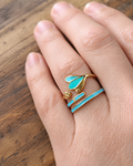 photo portée de gros plan sur le duo de bagues dorées en acier inoxydable composé d'une bague en finition laquée vert et turquoise en forme de feuille et d'un anneau en finition laquée turquoise. Cest un ensemble élégant et harmonieux sur le doigt.