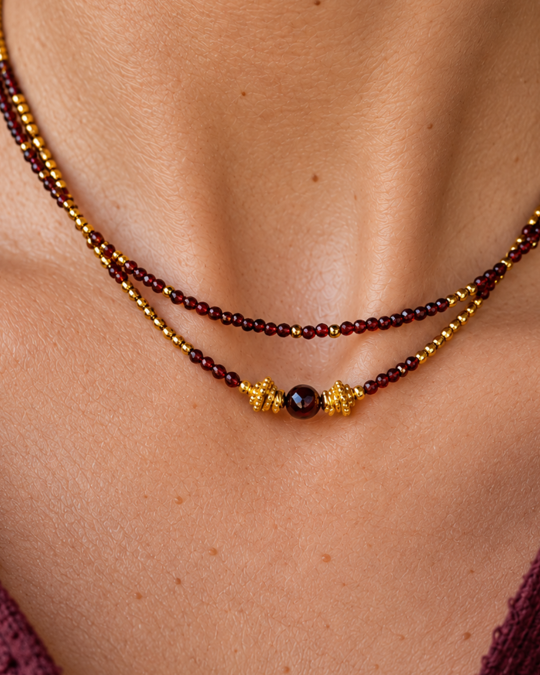 Gros plan sur le collier ras-du-cou double rang Les Heures Pourpres, mettant en valeur les grenats naturels facettés, l’hématite dorée et le motif central orné de perles travaillées en plaqué or 18 carats. Création de l’Atelier d’Yselia.