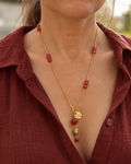 Sautoir Namasté porté sur une femme, composé d'une chaîne en plaqué or 18 carats, d'une cornaline rouge orangé, d'un pendentif Bouddha en hématite dorée et d'un médaillon martelé doré.