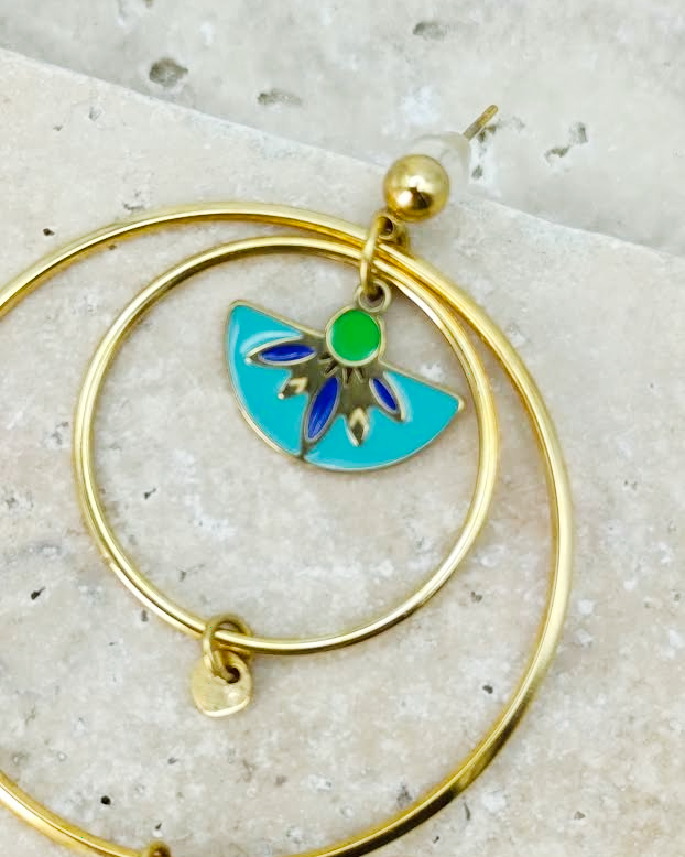 photo de gros plan sur les details du médaillon des boucles d'oreilles créoles dorées en acier inoxydable de la collection Santorin. On y voit la finesse des motifs et les nuances de vert, bleu et turquoise.