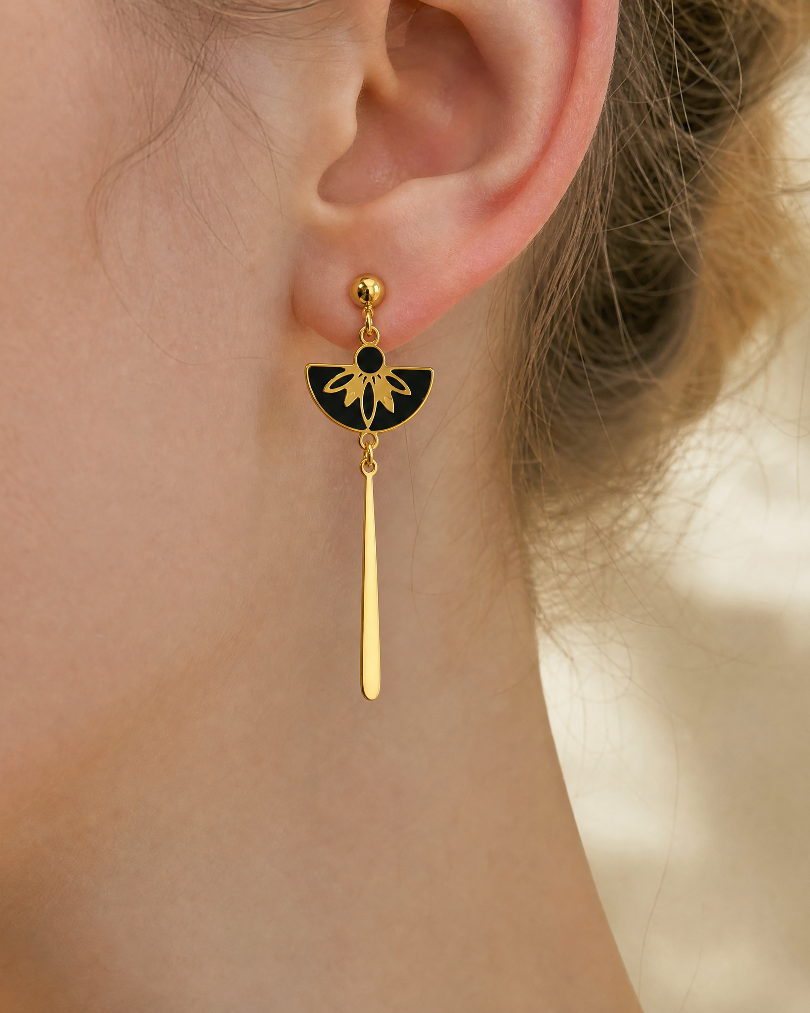 photo de gros plan sur les détails des boucles d'oreilles pendantes portées Palazzo, de la collection Venezia, en acier inoxydable doré avec des motifs laqués noirs. 